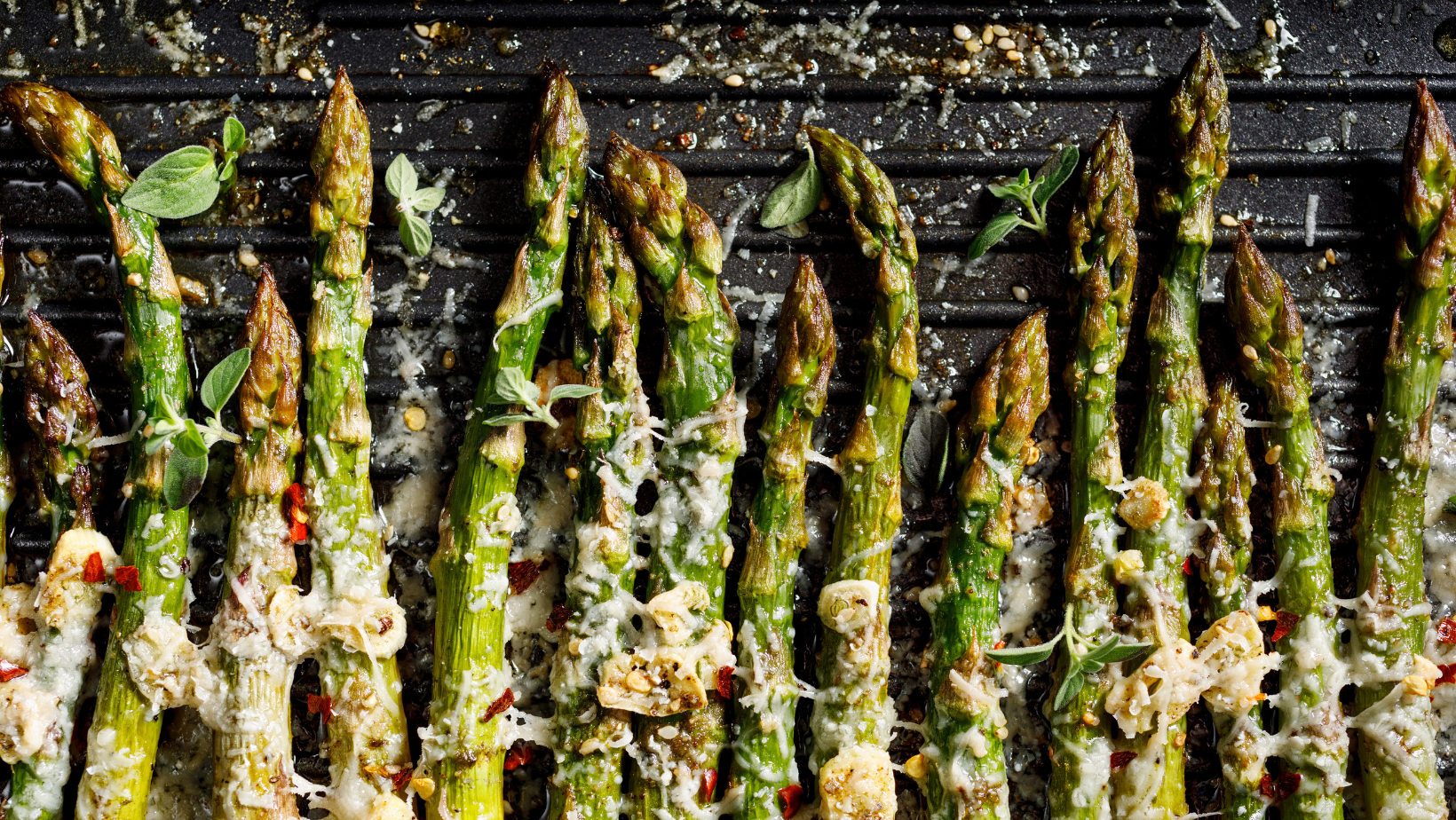 Grilled green asparagus with the addition of parmesan cheese, garlic and aromatic herbs on the grill plate, top view