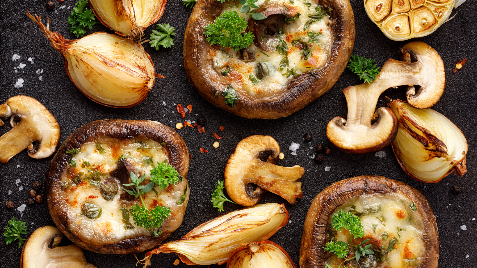 Stuffed portobello mushrooms stuffed with mozzarella and gorgonzola cheese and aromatic herbs on a black background, top view. Vegetarian food