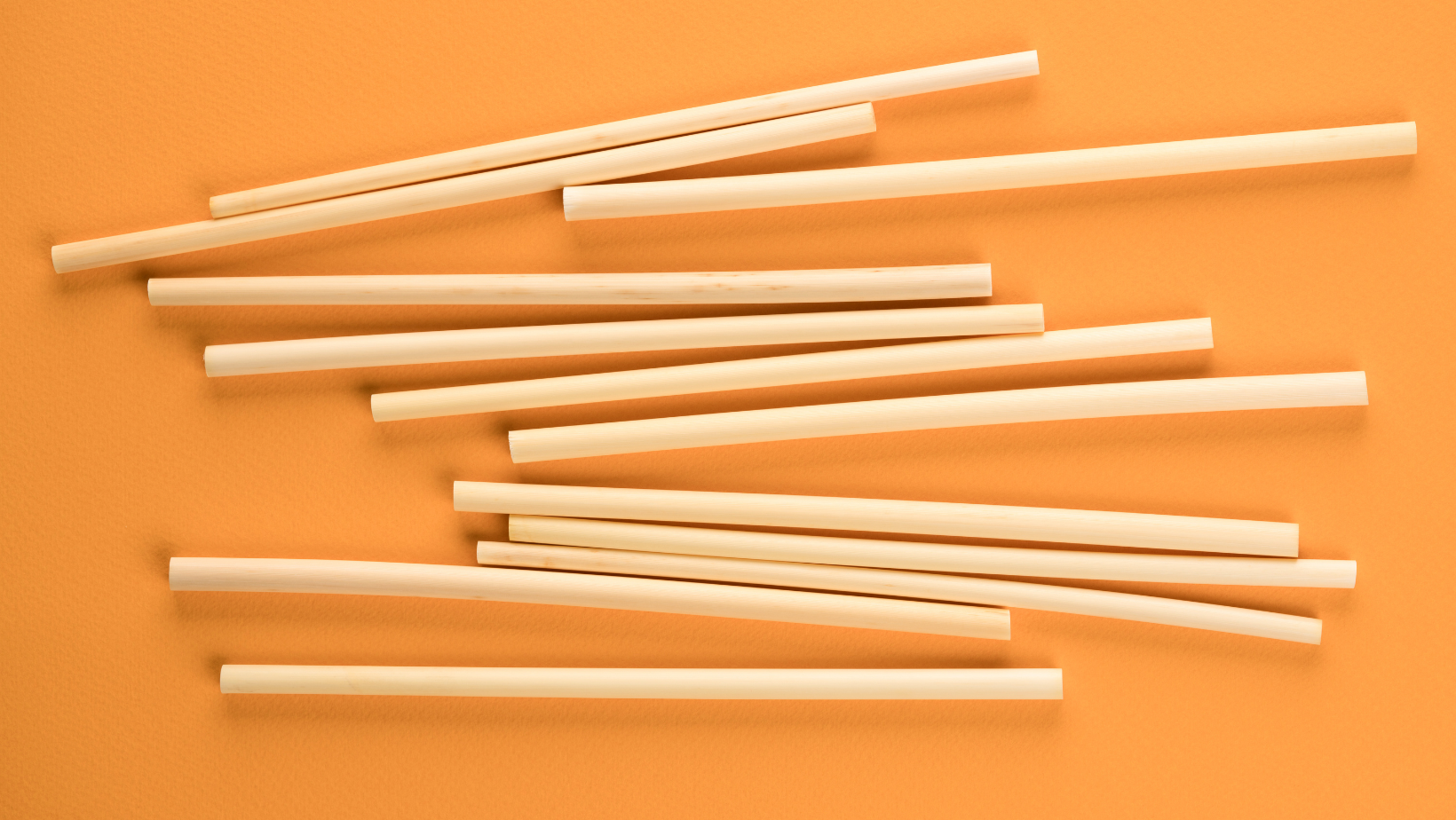 Natural biodegradable wheat drinking straws made of the stem of the wheat plant on orange background. Sustainable lifestyle and zero waste concept. Ethical consumerism. Flat lay