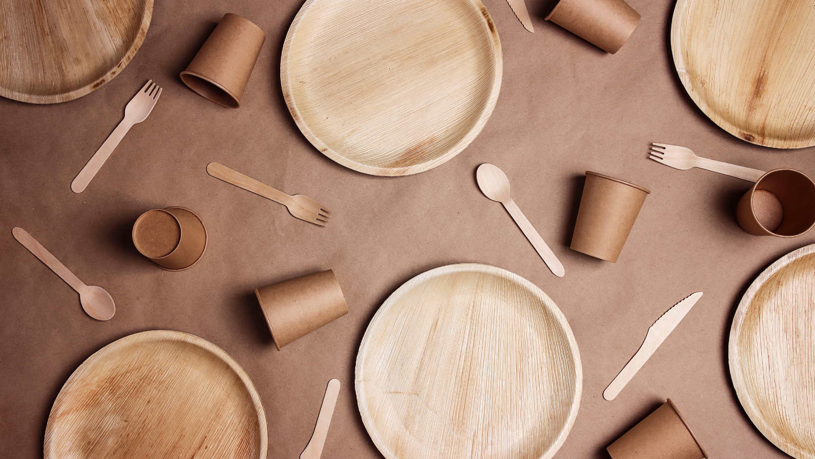 Flat lay composition with eco-friendly tableware on brown paper background. Bamboo plates, paper cups and wooden cutlery.
