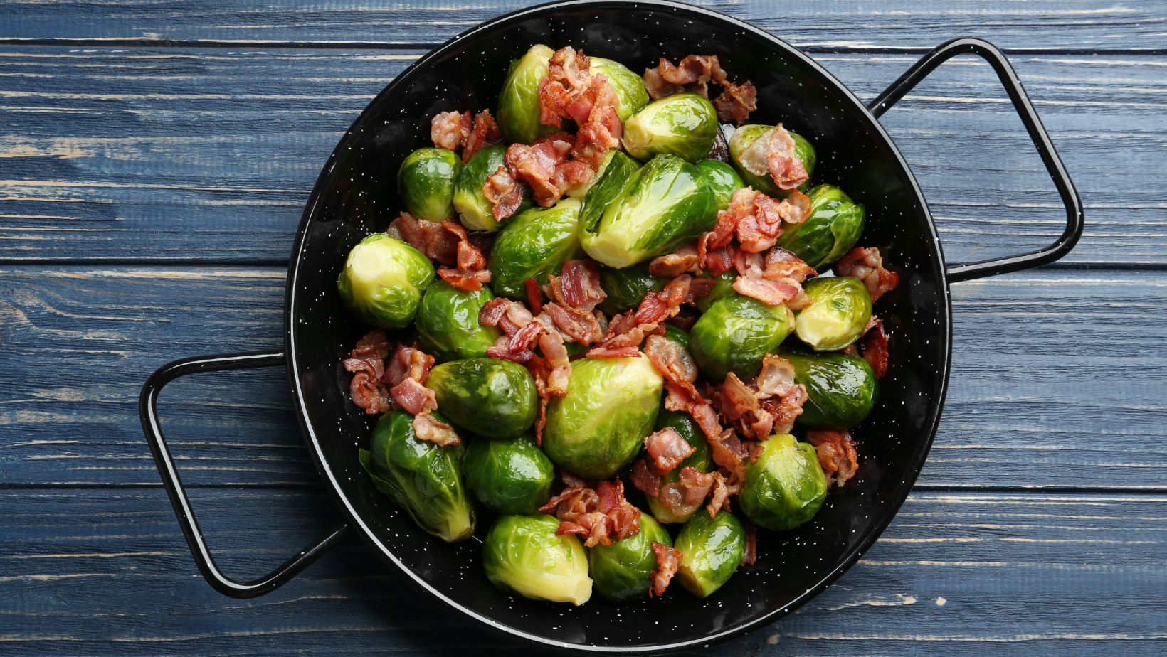 Tasty roasted Brussels sprouts with bacon on blue wooden table, top view