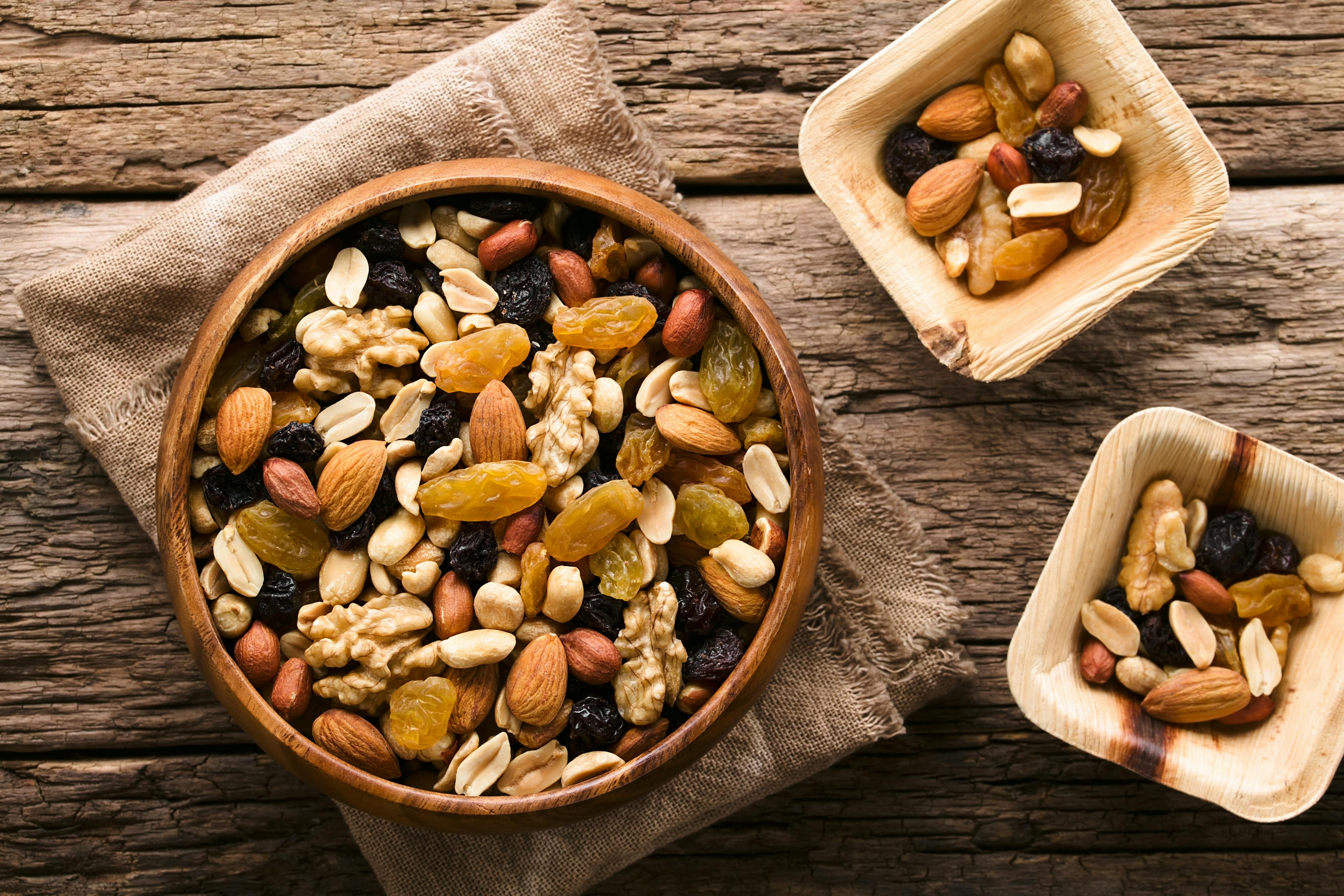 Healthy trail mix snack made of nuts (walnut, almond, peanut) and dried fruits (raisin, sultana) in wooden bowl, photographed overhead (Selective Focus, Focus on the trail mix in the big bowl) See Less